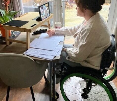 Woman sitting at her desk in her wheel chair, taking notes at home.