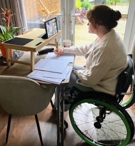 Woman sitting at her desk in her wheel chair, taking notes at home.