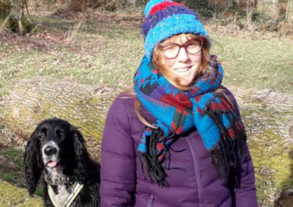 Holly, someone with a spinal cord injury who can walk without aids, sitting in a field with a dog