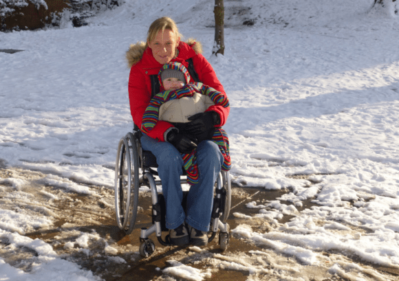 Clair, a spinal cord injured mum, holding her baby on her lap in a snowy field